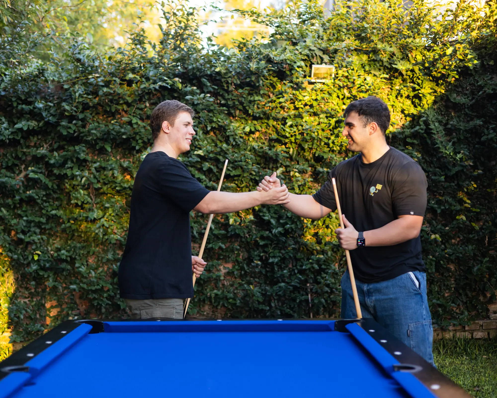 Dos amigos se saludan sobre una mesa de pool BlackSteel® de paño azul
