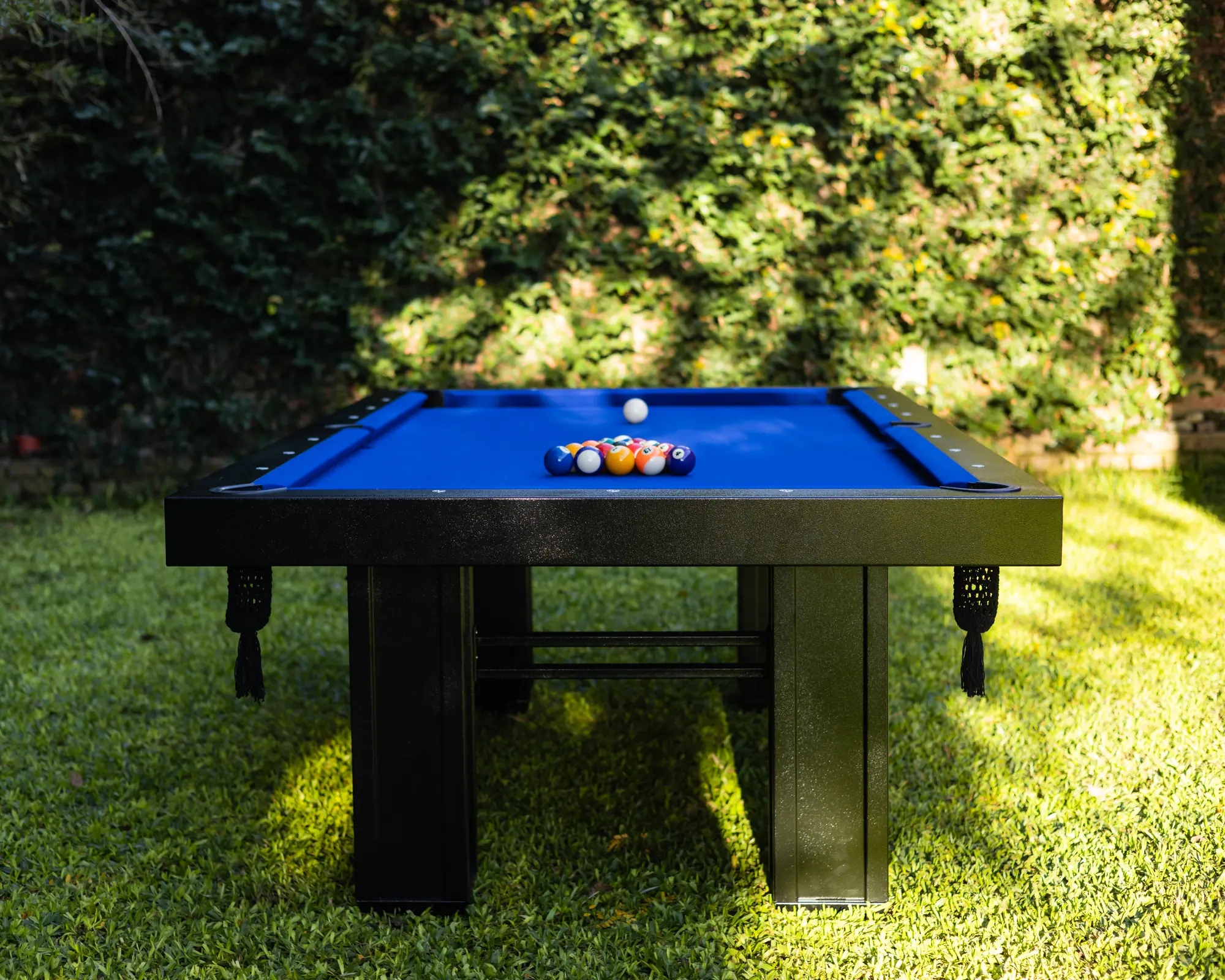 Mesa de pool BlackSteel® de paño azul en un jardín, con las bolas armadas